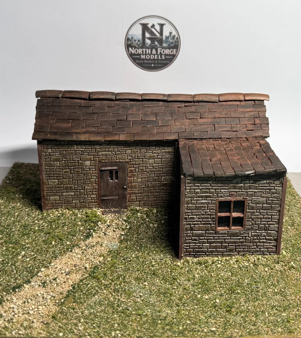 Single-storey L-shaped miniature stone house with weathered tiled roof